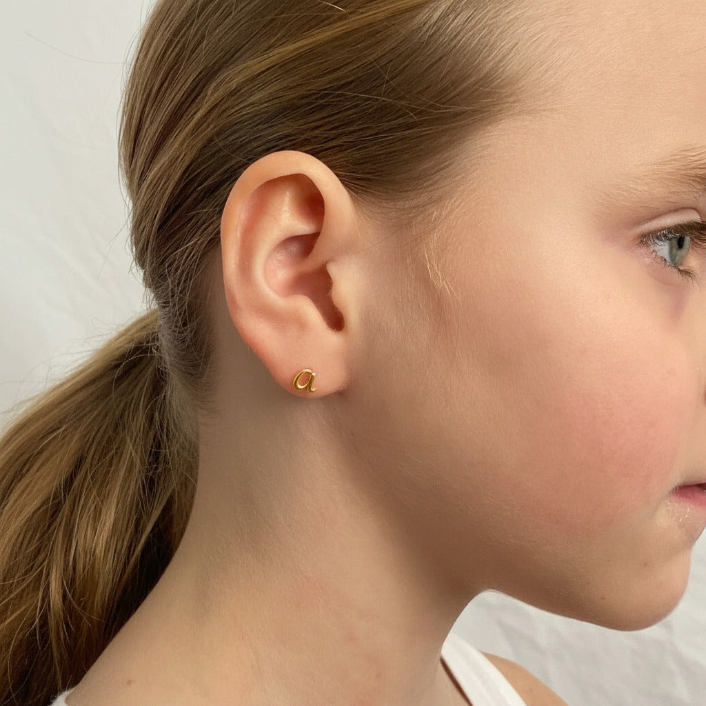 Closeup of a small girl wearing a gold initial stud earring