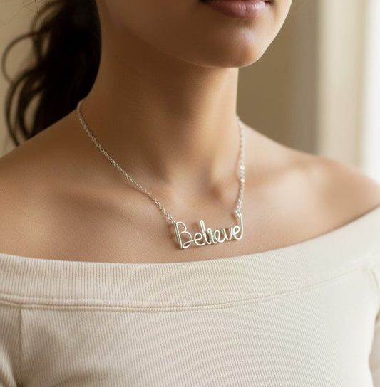 Woman wearing a silver necklace with the word 'Believe' on a neutral background