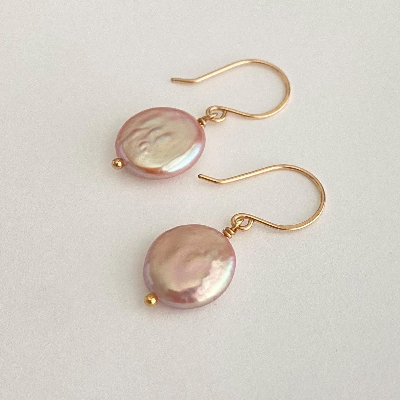 Pair of pink pearl earrings with gold hooks on a light gray background